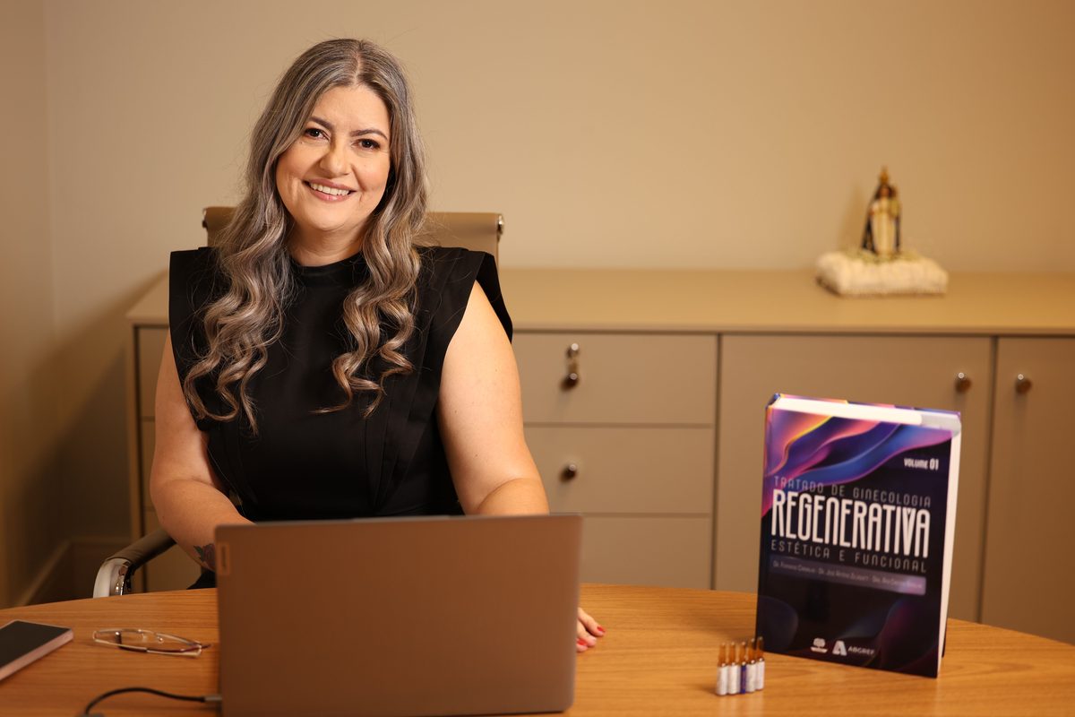Dra. Julienni Arvelos à mesa do consultório, com uma imagem de Nossa Senhora ao fundo